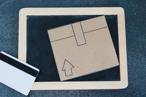 Cardboard parcel with blackboard and payment card on concrete desk 스톡 사진
