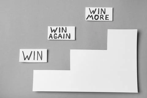 Cards with words WIN, WIN AGAIN, WIN MORE and paper cutout stairs on grey bac Foto stock