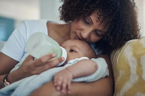 Care, woman feeding her baby with bottle and in living room on the sofa at their Stock Photos