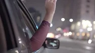 Carefree Young Woman Waves Hand In Breeze Out Moving Car Window In City At Night Stock Footage