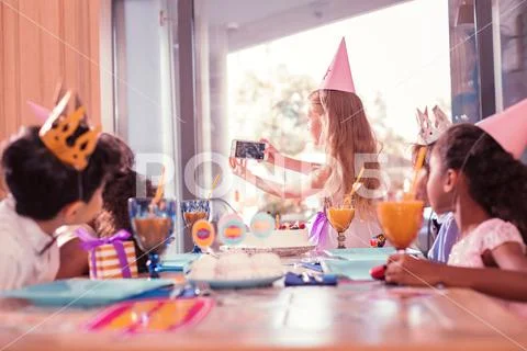 Careful birthday girl holding smartphone and taking selfies with friends Stock Photos