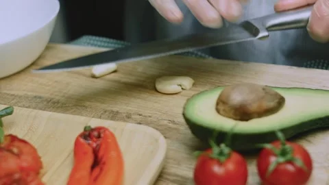 Careful culinary view of slicing garlic beside avocado and roasted vegetables Stock Footage 342152714