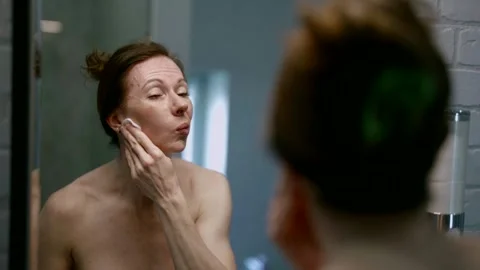 Carefully examining her reflection in the bathroom mirror, a middle-aged adult Stock Footage 276112554