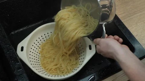 Carefully pouring the cooked spaghetti into a colander for draining Stock Footage 310518563