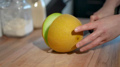 Carefully Slicing Fresh Yellow Melon on an Elegant Wooden Cutting Board Stock Footage 283486259