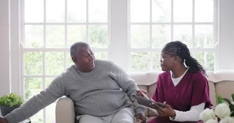 Caregiver coming with tablet consulting on sofa while patient putting phone down Video stock 345508847