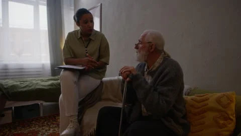 Caregiver Explaining Social Assistance Program to Elderly Man during Home Visit Stock Footage 329679947