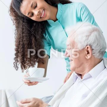 Caregiver giving senior man coffee Stock Photos