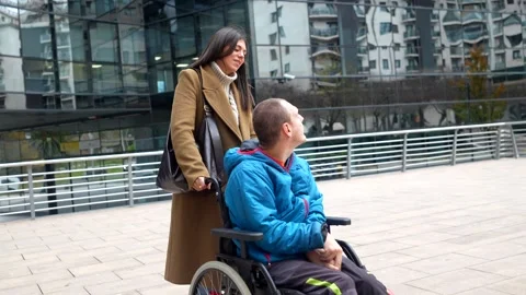 Caregiver pushing a young disabled man in wheelchair outdoors Stock Footage 325747723