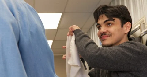 Carer helping a young man with a disability to do laundry at a launderette. 스톡 동영상 88374950