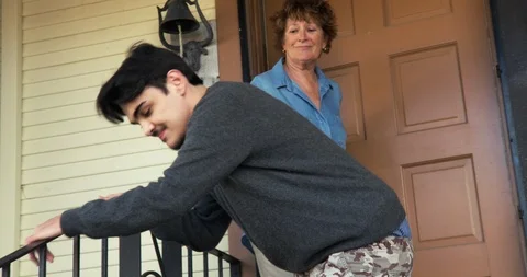 Carer helping a young man with a disability as he leaves the house. Vidéo 88374959