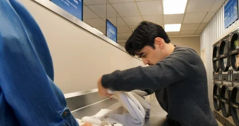 Carer helping a young man with a disability to do laundry at a launderette. 스톡 동영상 88375021