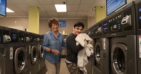 Carer helping a young man with a disability to do laundry at a launderette. Vidéo 88375058
