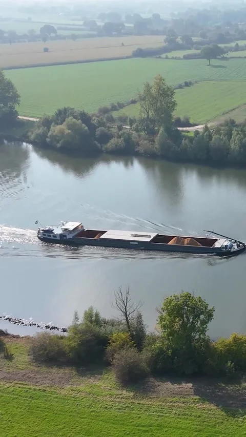 Cargo barge navigating river through green countryside Видео 327109198