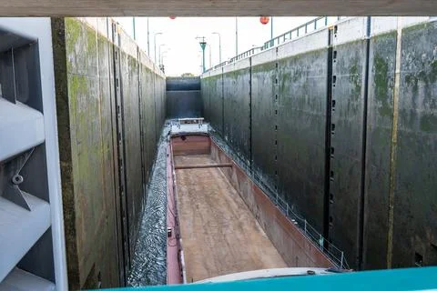 Cargo barge sitting inside a deep concrete canal lock chamber with algae stained Stock Photos