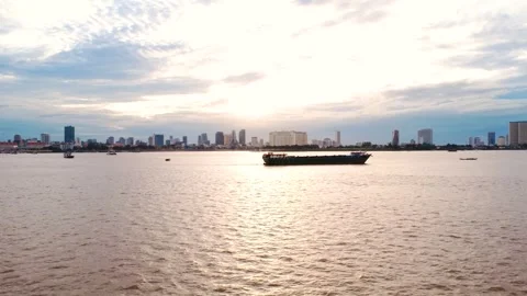 Cargo boat crossing the river at sunset in Phnom Penh, with Cambodia’s city Stock Footage 339860424
