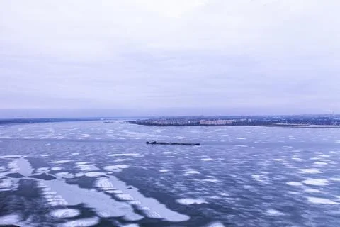 A cargo container ship moves along a frozen river. Stock Photos