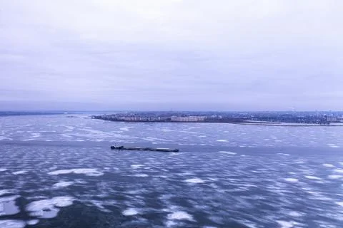 A cargo container ship moves along a frozen river. Stock Photos