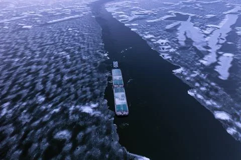 A cargo container ship moves along a frozen river. Stock-Fotos