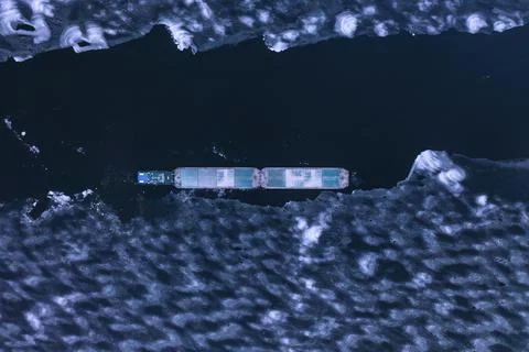 A cargo container ship moves along a frozen river. Stock Photos