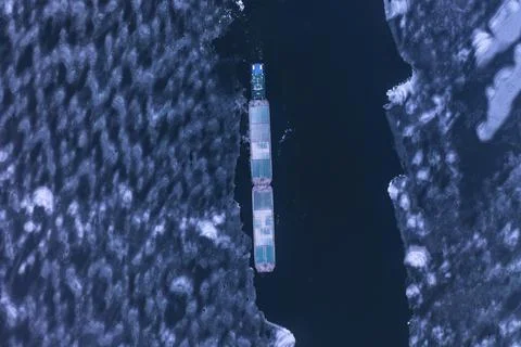 A cargo container ship moves along a frozen river. Stock Photos