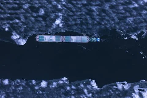 A cargo container ship moves along a frozen river. Stock Photos