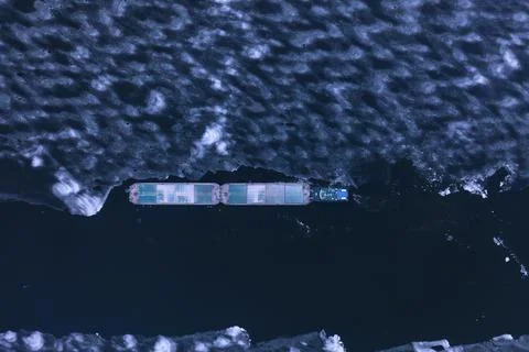 A cargo container ship moves along a frozen river. Stock Photos