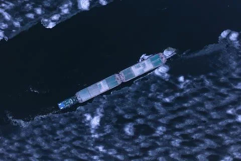 A cargo container ship moves along a frozen river. Stock Photos