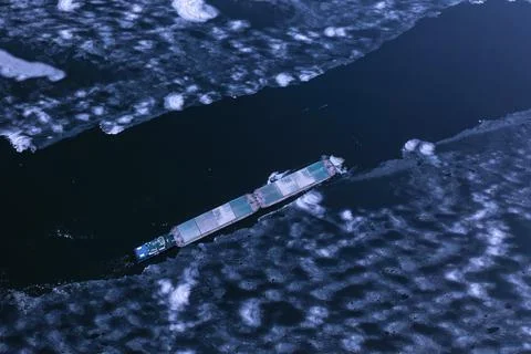 A cargo container ship moves along a frozen river. Stock Photos