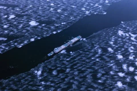A cargo container ship moves along a frozen river. Stock Photos