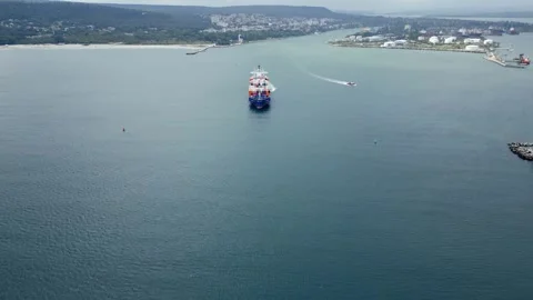 A cargo container ship navigates the harbor under a cloudy sky while a small Stock Footage 285513229