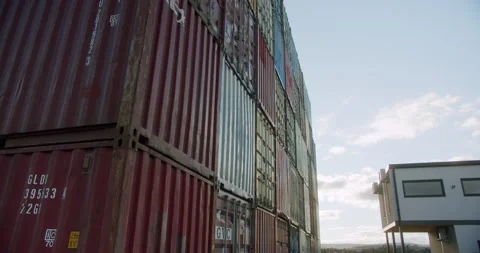 Cargo containers stacked at a shipping yard under a clear sky during afternoon Vídeos de archivo 327501664