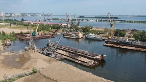 A cargo crane unloads sand from a barge at a river port on a sunny summer day Stock Footage 136525622