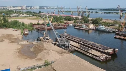 A cargo crane unloads sand from a barge at a river port on a sunny summer day Stock Footage 137029241