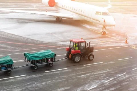 Cargo freight tractor machine delivering luggage carts to airplane at airport Stock-Fotos