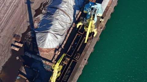 Cargo loading at a port with yellow cranes and a pile of material on the docks Stock Footage 335381504