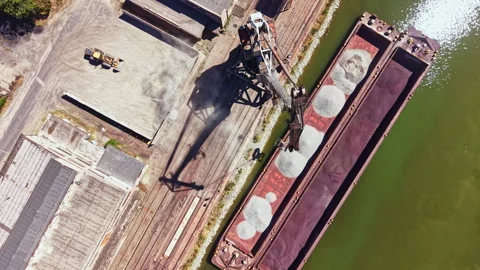Cargo loads are being transferred from a dock to a barge along a river in an Stock Footage 344089133