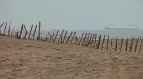Cargo ship across storm battered beach with wooden fence Stock Footage 1091998