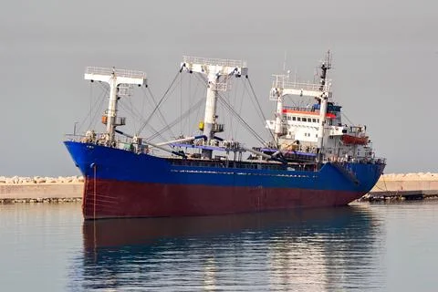 Cargo Ship with Blue and Red Hull Docked at Industrial Port Stock Photos
