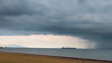 Cargo ship on calm sea under dramatic storm clouds and distant rain shower Stock Footage 340241674