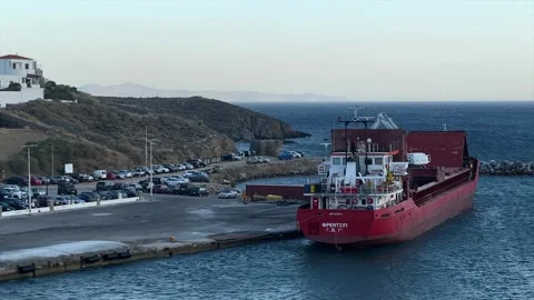 Cargo ship docked at a Greek harbor beside rocky coastline, vehicles, sea Stock Footage 346970260