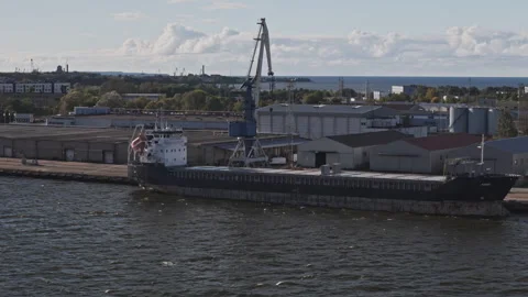 Cargo ship docked at port with crane and industrial buildings in background Vídeos de archivo 343485998