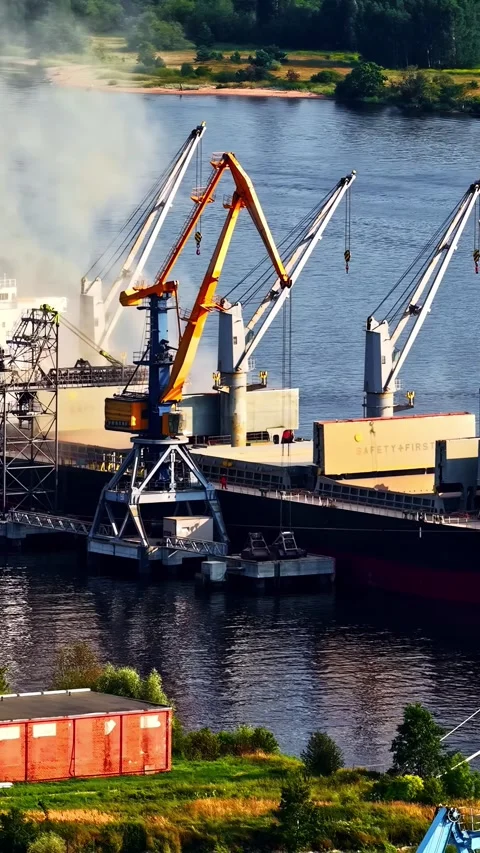 Cargo ship docked at riverside terminal with cranes loading freight for global 스톡 동영상 340322536