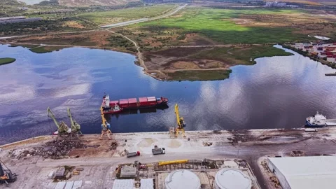Cargo ship docks at industrial port near water and green fields Stock Footage 339649519