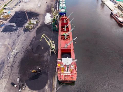 Cargo ship docks to load coal at a busy port during the day with equipment .. Stock Photos