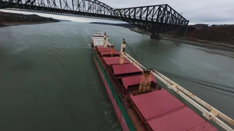 Cargo ship drifting through wide river valley under bridge 스톡 동영상 320588567