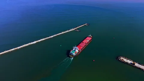 Cargo ship exiting harbor through concrete breakwater walls Stock Footage 331942146