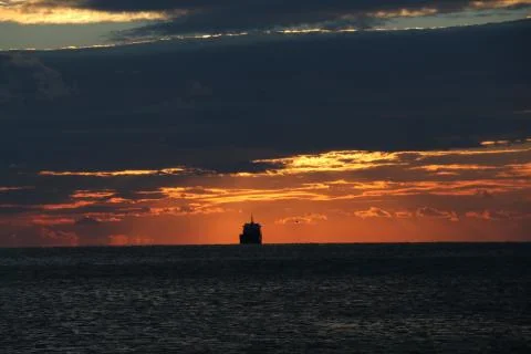 A cargo ship heading for the horizon at sunset and with the sky with clouds Stock Photos