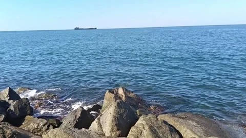 Cargo Ship on the Horizon of a Calm Blue Sea with Rocky Shore Stock Footage 343014672