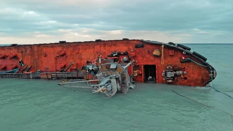 Cargo ship lies on its side, near the shore of a sandy beach with a barrier to Stock Footage 121438451